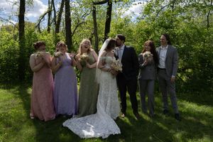 Wedding party with bridesmaids in colorful gowns celebrating couple kissing outdoors.