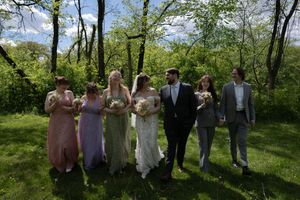 Wedding party walks together through a sunny green garden, bridesmaids in pastel gowns holding bouquets.