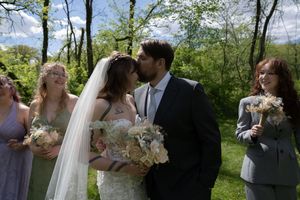 Bride and groom share first kiss surrounded by bridesmaids in lavender dresses at outdoor wedding.
