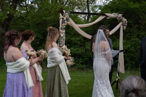 Bridesmaids in pastel dresses standing beside bride at floral outdoor wedding arch.