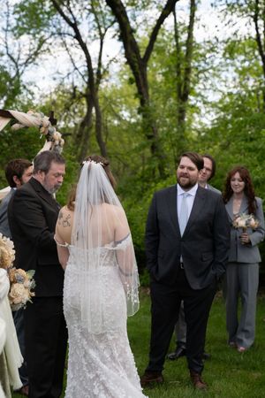 Groom smiles warmly as bride approaches him at the altar during an outdoor garden wedding ceremony.