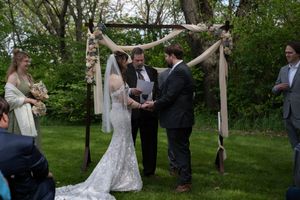 Bride and groom exchange vows under a rustic floral arch during an intimate outdoor wedding ceremony in a wooded setting.