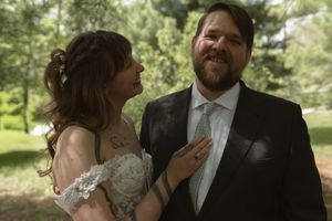 Bride adjusting groom's tie while smiling at him during outdoor wedding portrait session.