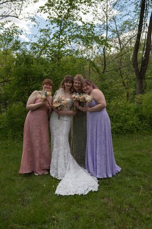 Bride posing with three bridesmaids in pink and lavender dresses in garden setting.