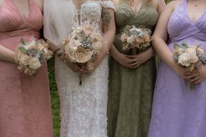 Bride and three bridesmaids in pastel gowns hold bouquets of neutral-toned flowers at wedding.