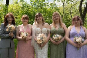 Bride with four bridesmaids in colorful gowns holding bouquets in garden setting.