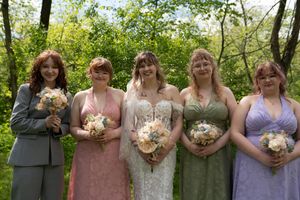 Bride in lace gown with four bridesmaids in colorful dresses holding bouquets outdoors in spring.