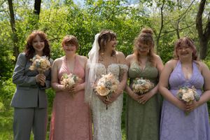 Smiling bride with veil poses with four bridesmaids in colorful dresses in a lush garden setting.
