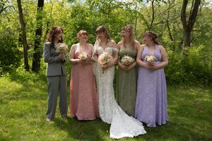 Bride and four bridesmaids laughing together outdoors in colorful dresses with bouquets.