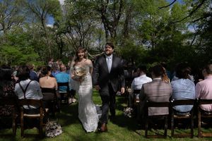 Bride and groom walk back down the aisle after their outdoor wedding ceremony surrounded by seated guests.