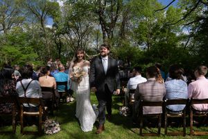 Newlyweds walk hand in hand down the aisle after outdoor wedding ceremony with seated guests.