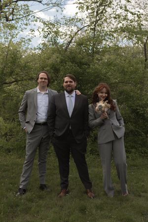 Groom with two wedding party members in matching gray suits posing in a lush green garden.