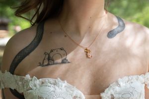 Close-up of bride's Totoro chest tattoo and delicate gold cross necklace on wedding day.