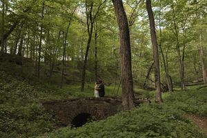 Bride and groom share romantic moment on stone bridge surrounded by lush green forest trees.