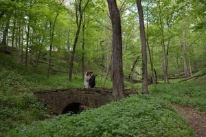 Newlyweds sharing a romantic moment on a stone arch bridge surrounded by lush forest.