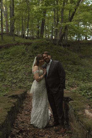 Bride and groom pose together on stone steps surrounded by lush green forest in romantic wedding portrait.