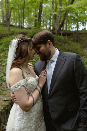 Bride and groom sharing an intimate forehead touch moment in a lush green forest setting.