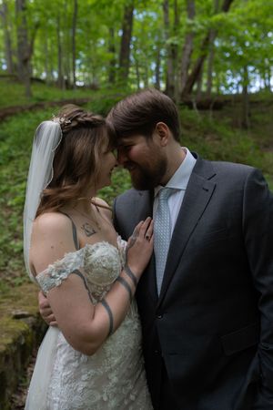 Bride and groom share an intimate forehead touch moment surrounded by lush green forest.