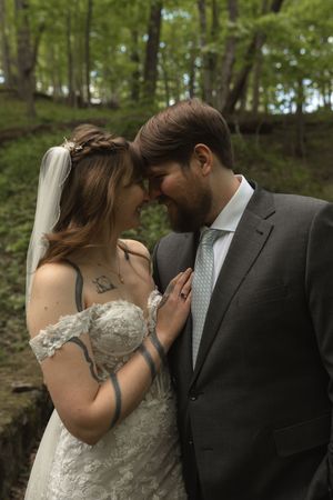 Bride and groom touch foreheads tenderly in a romantic woodland wedding portrait.
