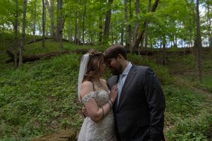 Newlyweds share intimate forehead-to-forehead moment surrounded by lush green forest backdrop.