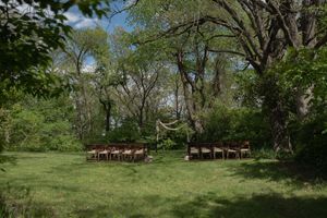 Empty outdoor wedding ceremony setup with wooden chairs and floral arch in a green meadow.