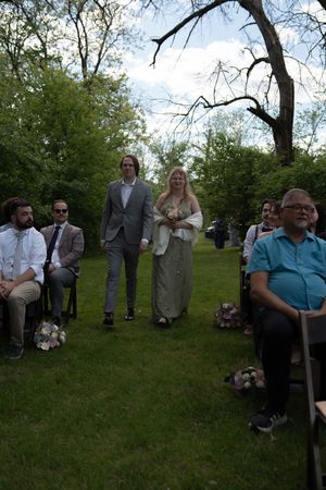 Bride and escort walk down the outdoor aisle past seated wedding guests during a garden ceremony.