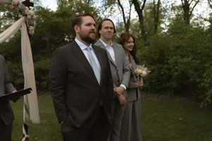 Wedding guests stand outdoors near floral arch during outdoor garden ceremony.