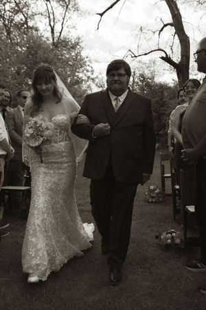 Black and white photo of bride in lace gown walking down outdoor aisle with father of the bride.