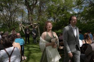 Smiling bride in white dress and groom in gray suit walk back down the aisle after outdoor garden wedding ceremony.