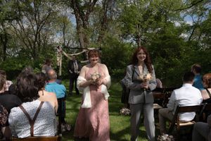 Two women in pink and gray walk down the aisle smiling during an outdoor spring wedding ceremony.