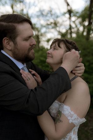 Groom in dark suit tenderly holds brides face as they share an intimate moment outdoors at dusk.