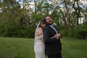 Bride in lace wedding dress embraces bearded groom in black suit during romantic outdoor wedding portrait session.
