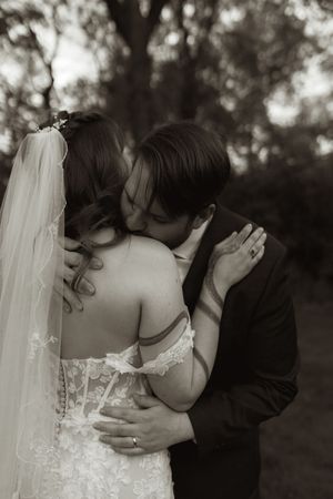 Black and white photo of bride and groom sharing a romantic kiss outdoors on their wedding day.