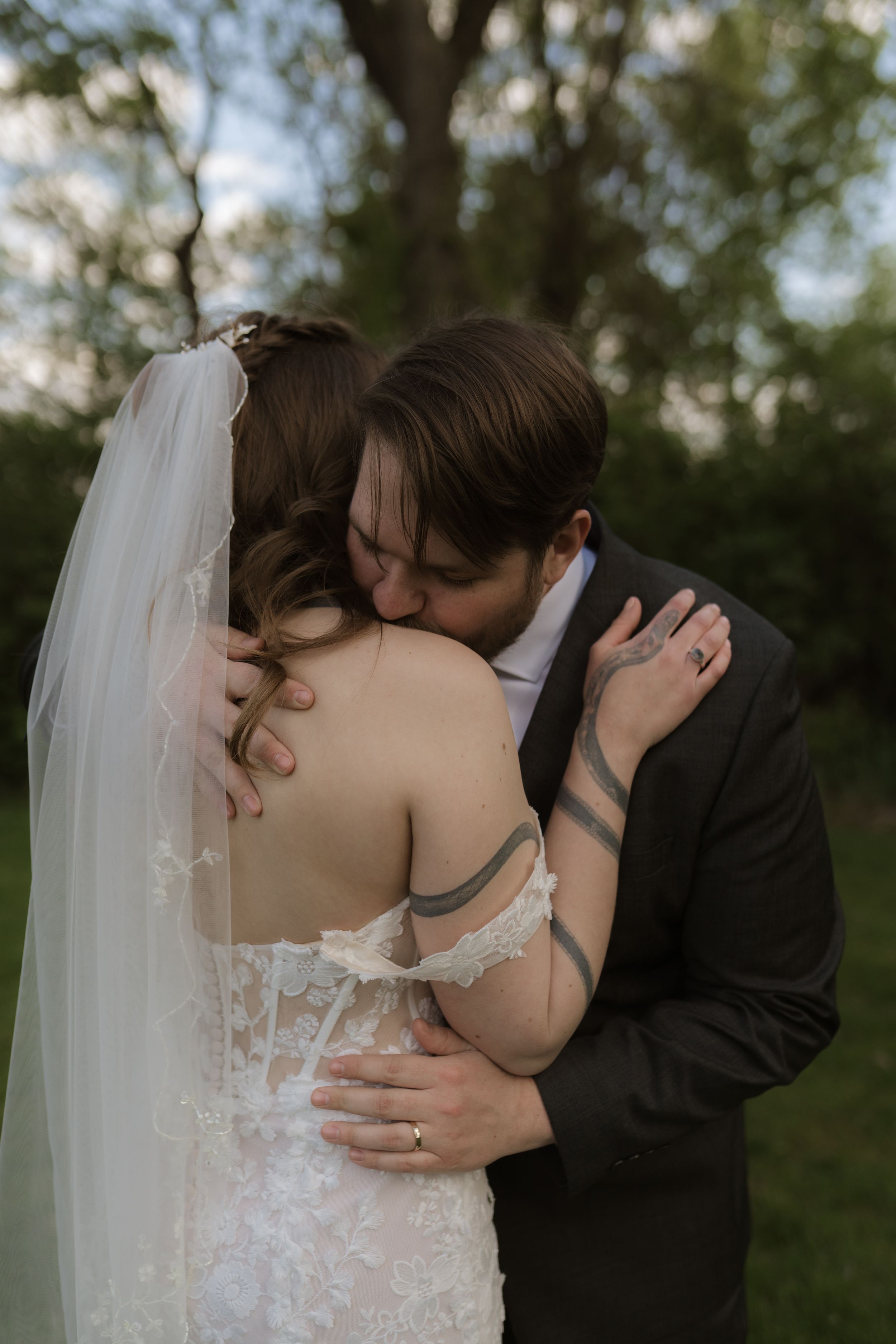 Bride and groom sharing an intimate embrace and kiss outdoors, bride wearing lace wedding dress with veil.
