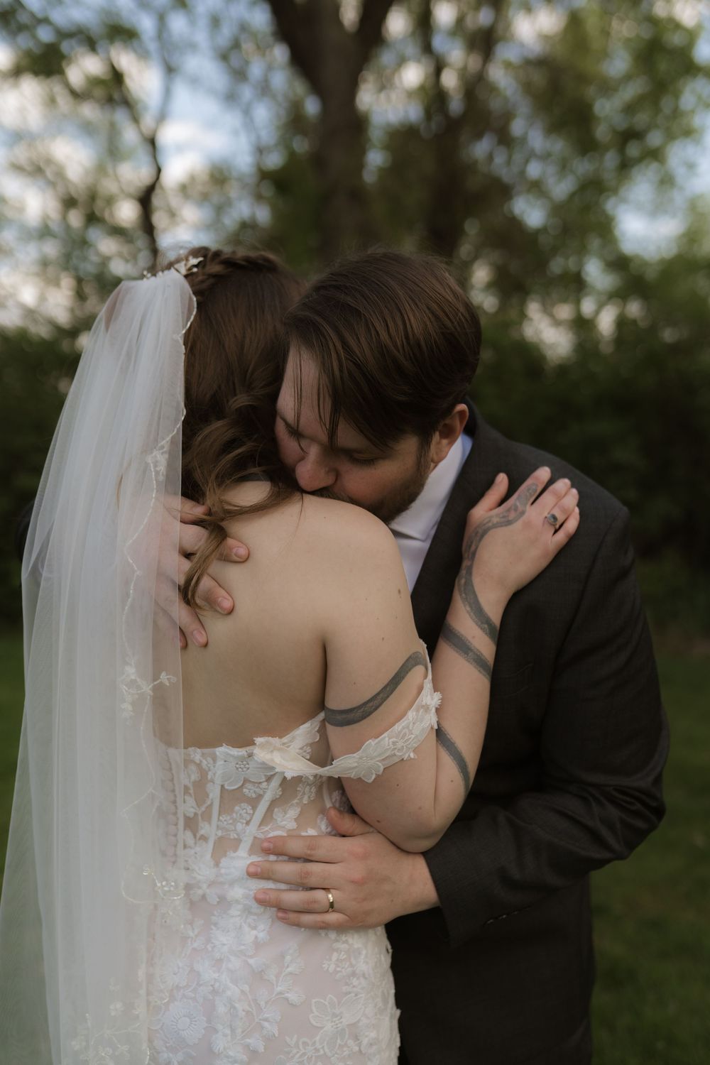 Bride and groom sharing an intimate embrace and kiss outdoors, bride wearing lace wedding dress with veil.