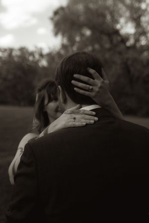Black and white photo of bride embracing groom from behind showing wedding ring.