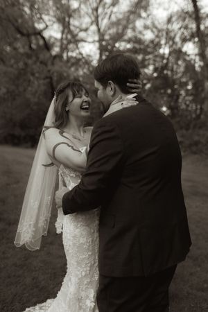Black and white photo of laughing bride and groom sharing joyful moment during outdoor wedding.