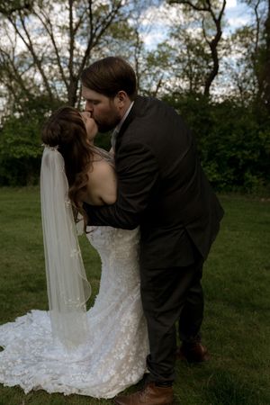 Bride and groom sharing a romantic dip kiss on a green lawn with trees in the background.