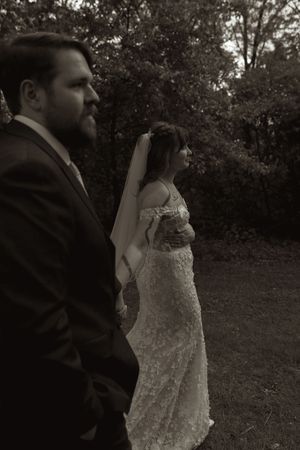 Black and white portrait of bride in lace gown and groom in suit standing outdoors.