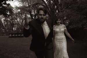 Bride and groom walking together outdoors in black and white wedding photo among trees.