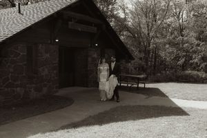 Bride and groom posing together outside rustic stone building in black and white wedding photo.