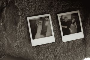 Two vintage Polaroid photos of wedding couples displayed on a textured stone wall in black and white.
