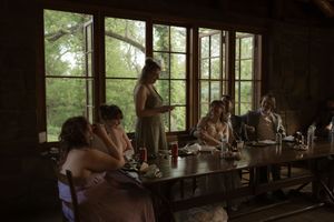 Wedding party gathered around a rustic wooden table inside a lodge with large windows overlooking trees.
