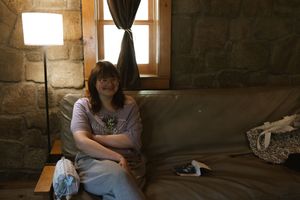 Woman sitting relaxed on a couch in a rustic stone room with warm lamp light and a small window.