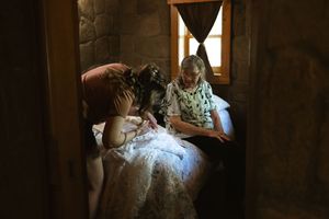 Bride getting ready in rustic stone room with loved ones helping with wedding dress details.