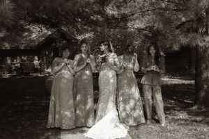 Bride and four bridesmaids posing together under trees in black and white wedding photo.