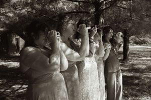 Bridesmaids in formal dresses photograph outdoors under pine trees in a black and white wedding photo.