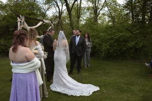 Outdoor wedding ceremony with bride, groom, and officiant wearing antler headdress on grass.