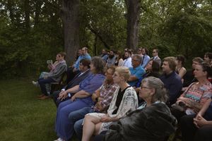 Guests seated outdoors at a wedding ceremony surrounded by lush green trees.