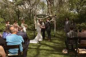 Outdoor wedding ceremony under rustic arch with bride and groom exchanging vows among seated guests.